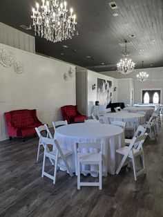 an empty banquet room with white tables and red couches, chandeliers and chairs