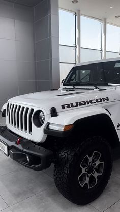 a white jeep is parked in a showroom with large windows on the wall behind it