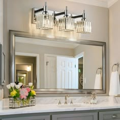 a bathroom vanity with a large mirror above it and flowers in a vase on the counter