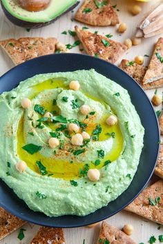 hummus with chickpeas and avocado in a blue bowl surrounded by crackers