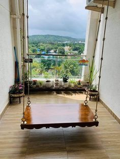 a wooden swing sitting on top of a hard wood floor next to a window filled with potted plants