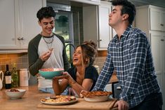 three people standing around a kitchen counter eating food