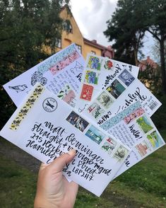 someone is holding up some letters and envelopes in front of a house with trees