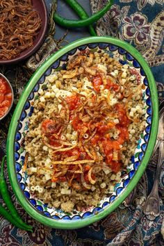 a bowl filled with food next to two bowls of chili sauce and green peppers on the side