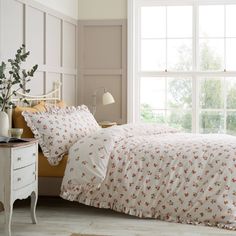 a bed sitting next to a window covered in white sheets and pillow cases on top of a wooden floor