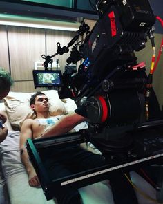 a man laying in bed next to a camera set up on top of a table