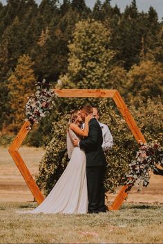 a bride and groom kissing in front of a wooden arch