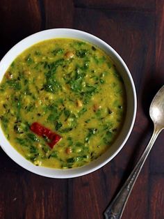 a white bowl filled with green soup next to a spoon on top of a wooden table