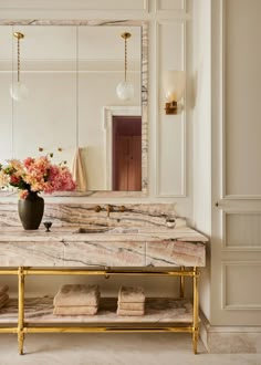 a bathroom with a marble counter top and gold accents on the mirror above it is a vase with flowers