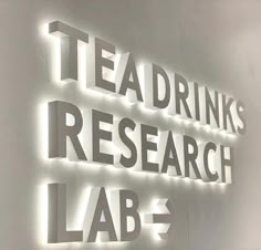 the words tea drink research lab are lit up in front of a wall with white letters