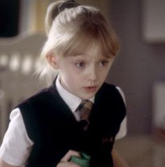 a young blonde girl wearing a black vest and tie holding a green object in her hands