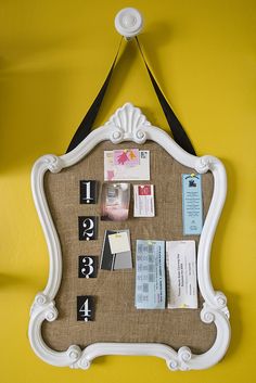 a white frame hanging on the side of a yellow wall filled with cards and magnets