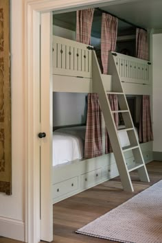 bunk beds with ladders and curtains are in the corner of a room that is painted white