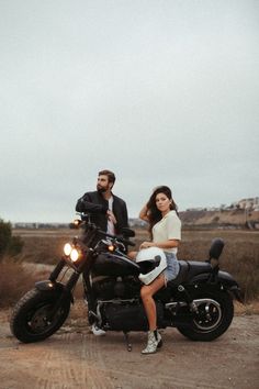 a man and woman sitting on a motorcycle in the middle of a dirt road,