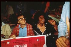 two men sitting next to each other in front of a crowd holding up a red and white checkered movie ticket