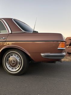 an old brown car parked on the side of the road in front of some rocks