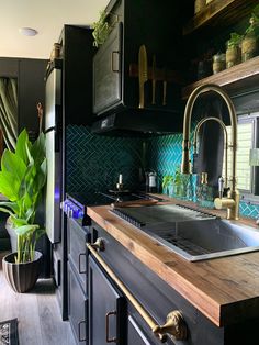 a kitchen with wooden counter tops and black cabinets, green tile backsplash and brass faucets