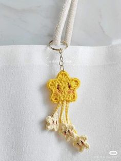 a crocheted keychain hanging from a white bag with a yellow flower on it