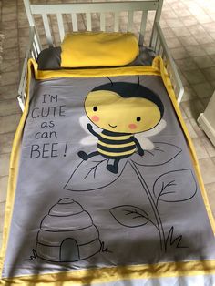 a baby bed with a yellow and gray blanket on it's side that says i'm cute as can bee