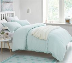 a bed with blue comforters and pillows in a white room next to a window