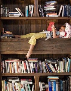 a young boy laying on top of a book shelf filled with books