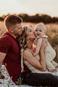 a man and woman are sitting on the ground with their baby in their lap while they kiss each other