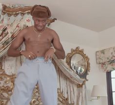 a shirtless man standing on top of a bed in front of a mirror and curtains