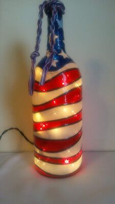 a red, white and blue striped glass bottle with string lights on the top is sitting on a table