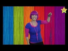 a woman with pink hair is standing in front of rainbow colored wall and pointing at the camera