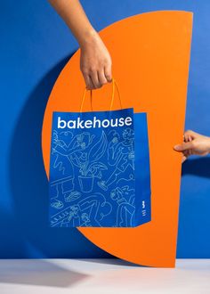 a person holding a blue bag with the word bakehouse on it and an orange background