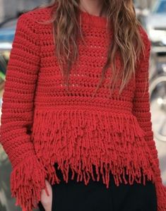 a woman is wearing a red sweater with fringes on her shoulders and black pants