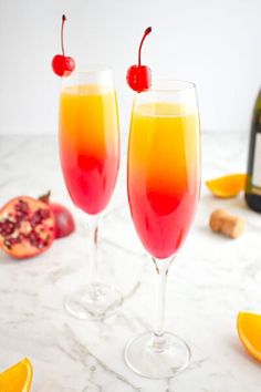 two wine glasses filled with orange and raspberry punch on a marble counter top