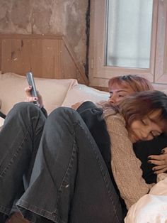 two women sitting on a bed with their arms around each other and one holding a cell phone