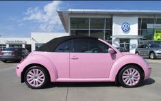 a pink car parked in front of a volkswagen dealership