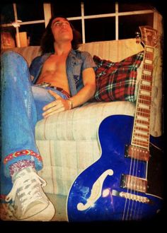 a man laying on top of a couch next to an electric guitar and another blue guitar