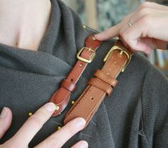 a woman wearing a brown leather watch band with gold buckles on her wrist and holding onto the strap