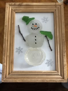 a snowman made out of sea glass in a frame on a table with other items