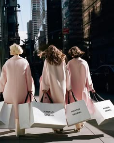 three women in pink coats are carrying shopping bags down the street with their backs to the camera