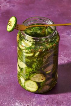 a jar filled with pickles and cucumbers next to a wooden utensil