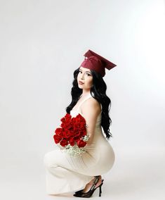 a woman in a graduation cap and gown kneeling down with flowers on her lap, holding a bouquet of red roses