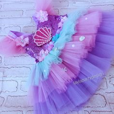 a purple and blue tutu skirt with a heart on the front, sitting against a brick wall