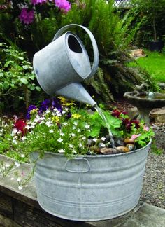 a watering can filled with flowers and water pouring out of it's top into a garden