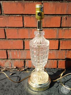 an old fashioned glass lamp sitting on top of a stone floor next to a brick wall