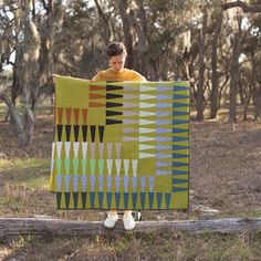 a woman holding up a quilt in the woods