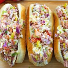 three hot dogs on buns covered in coleslaw and relish sitting on a cutting board