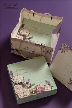 an open box with flowers on it sitting on a purple surface next to two cards