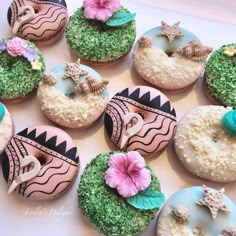 many decorated doughnuts on a table with flowers and seashells around them