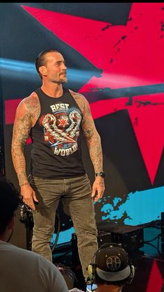 a man standing on top of a stage wearing a black shirt and hat with tattoos