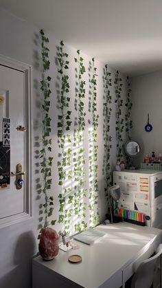 a room with white walls and green plants on the wall, along with a desk