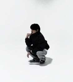 a young boy squatting on the ground in front of a white background wearing black shoes